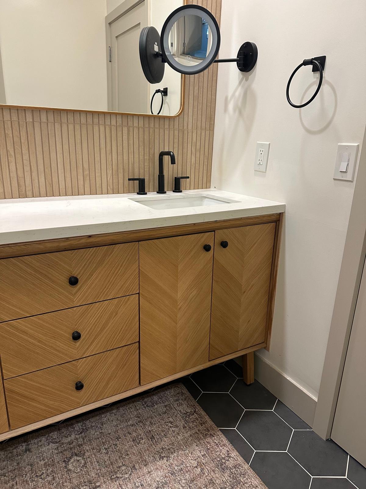 Bathroom with a chevron wood vanity and black hexagon floor by Jill Seidner Interior Design