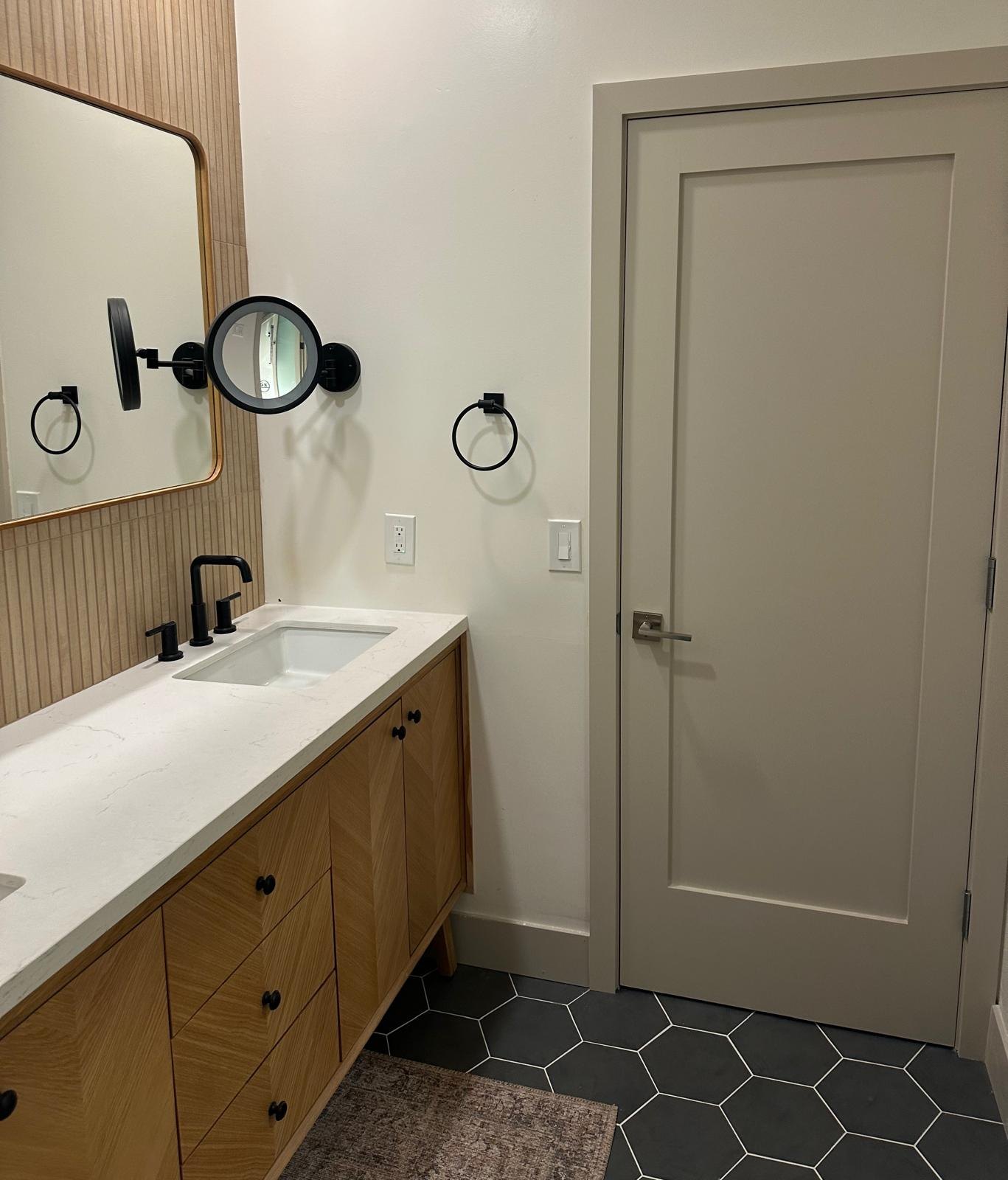 Bathroom with a wood vanity and a black hexagon tile floor by Jill Seidner Interior Design
