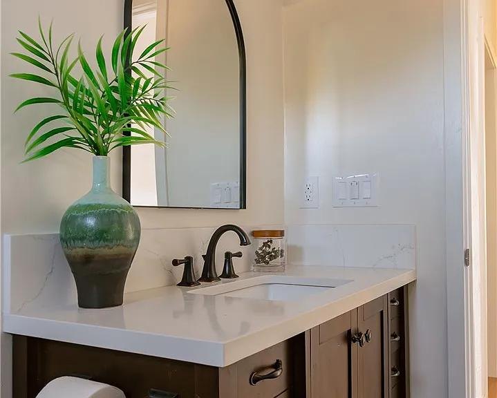 Bathroom with a wood vanity, an arched mirror and a black faucet by Jill Seidner Interior Design