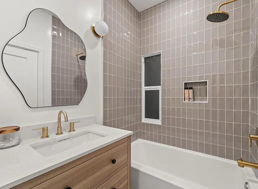 Bathroom with a curved mirror, gray tile and a soaking tub by Jill Seidner Interior Design