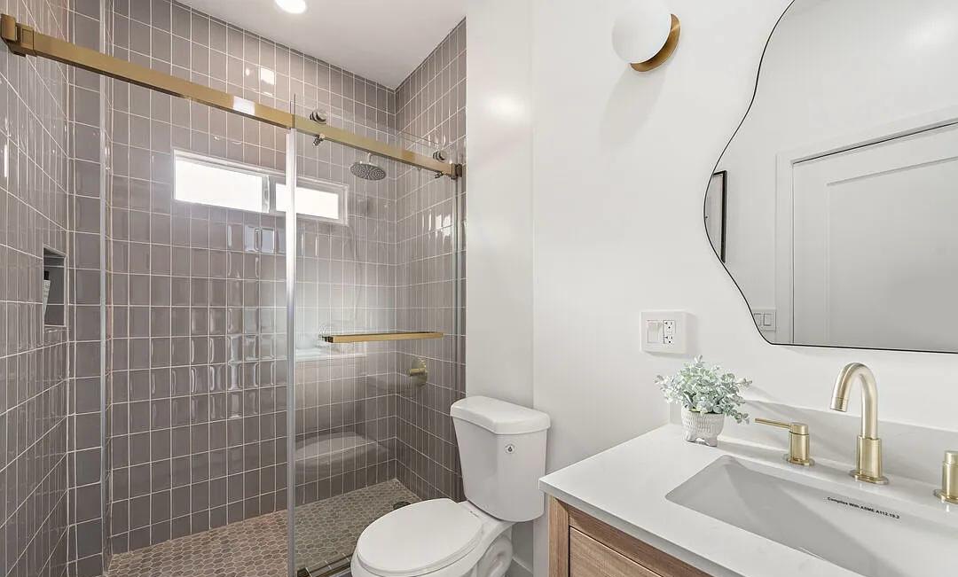 Bathroom with gray tile, a glass shower and a curved mirror by Jill Seidner Interior Design