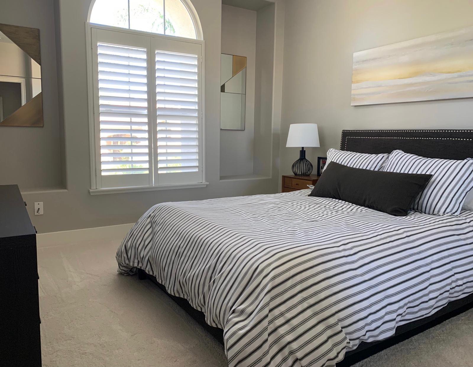 Bedroom with a striped duvet and window shutters by Jill Seidner Interior Design