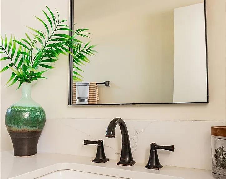 Bathroom vanity detail with a black faucet and a green vase by Jill Seidner Interior Design