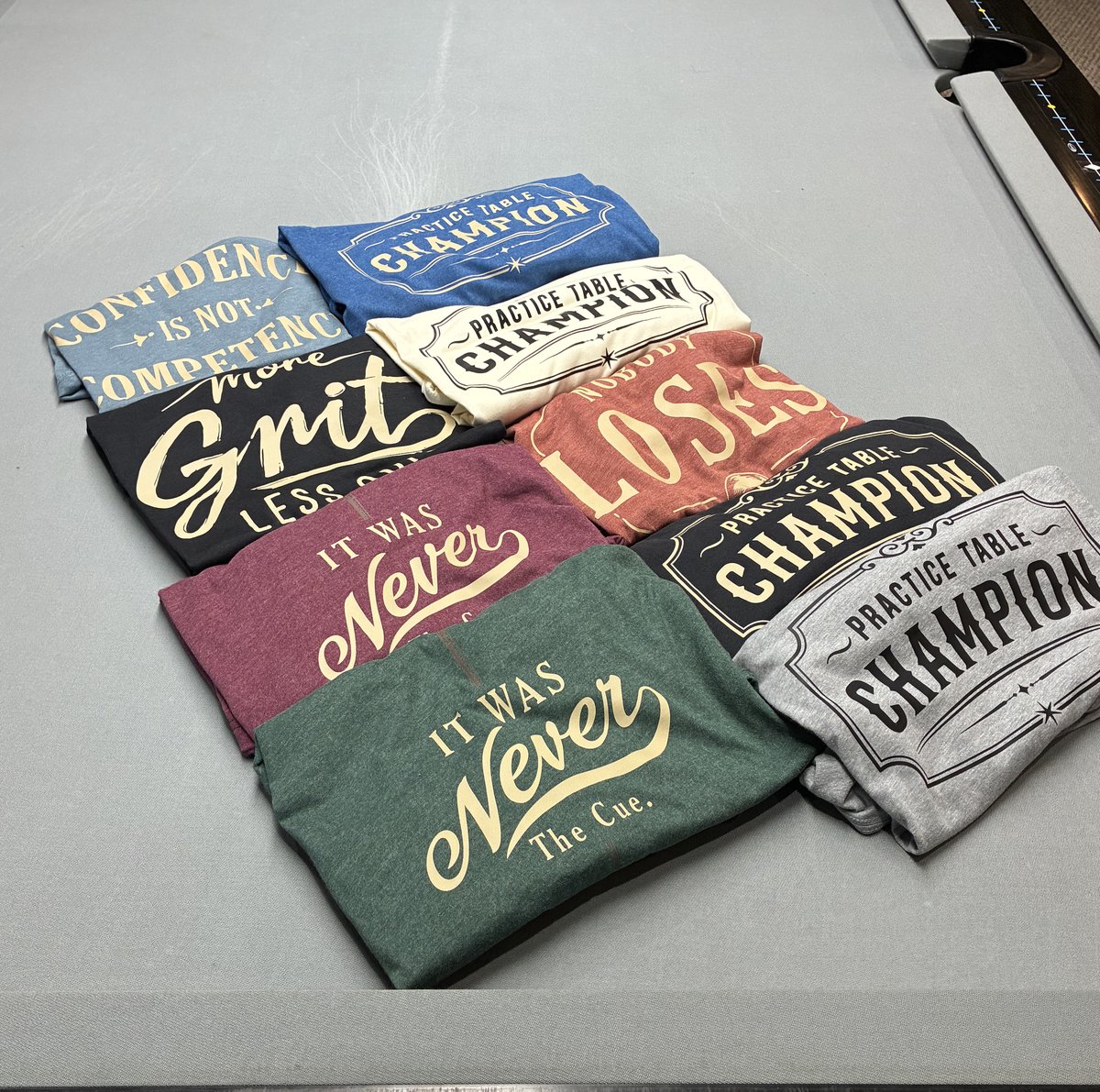 Folded PTC shirts arranged on a pool table.