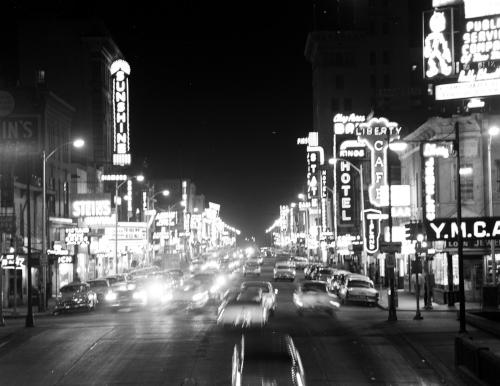 High contrast night photograph hovering over a street with neon signs like hotel and YMCA along the signs. Four lanes of traffic.