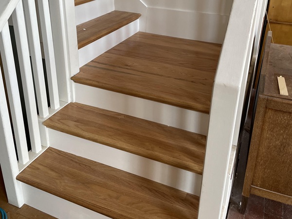 Staircase renovation featuring new wood stairs replacing worn carpet, new balustrade, freshly painted.