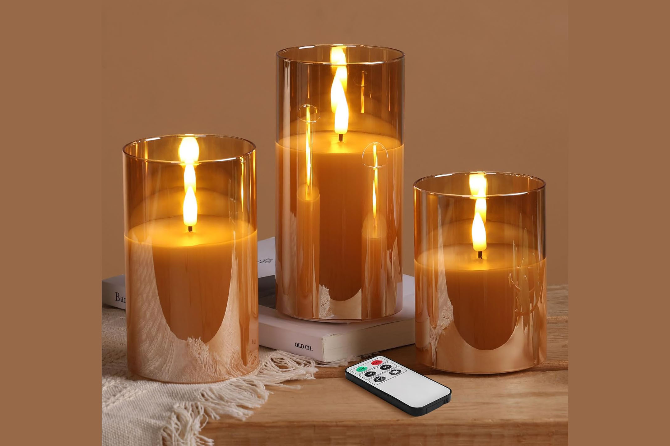 Three flameless pillar candles in warm gold glass cylinders of graduated heights.