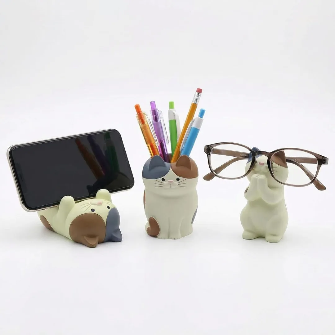 A set of three cat desk organizers: one is holding a phone, one is holding pencils & pens, and another is holding a pair of eyeglasses.