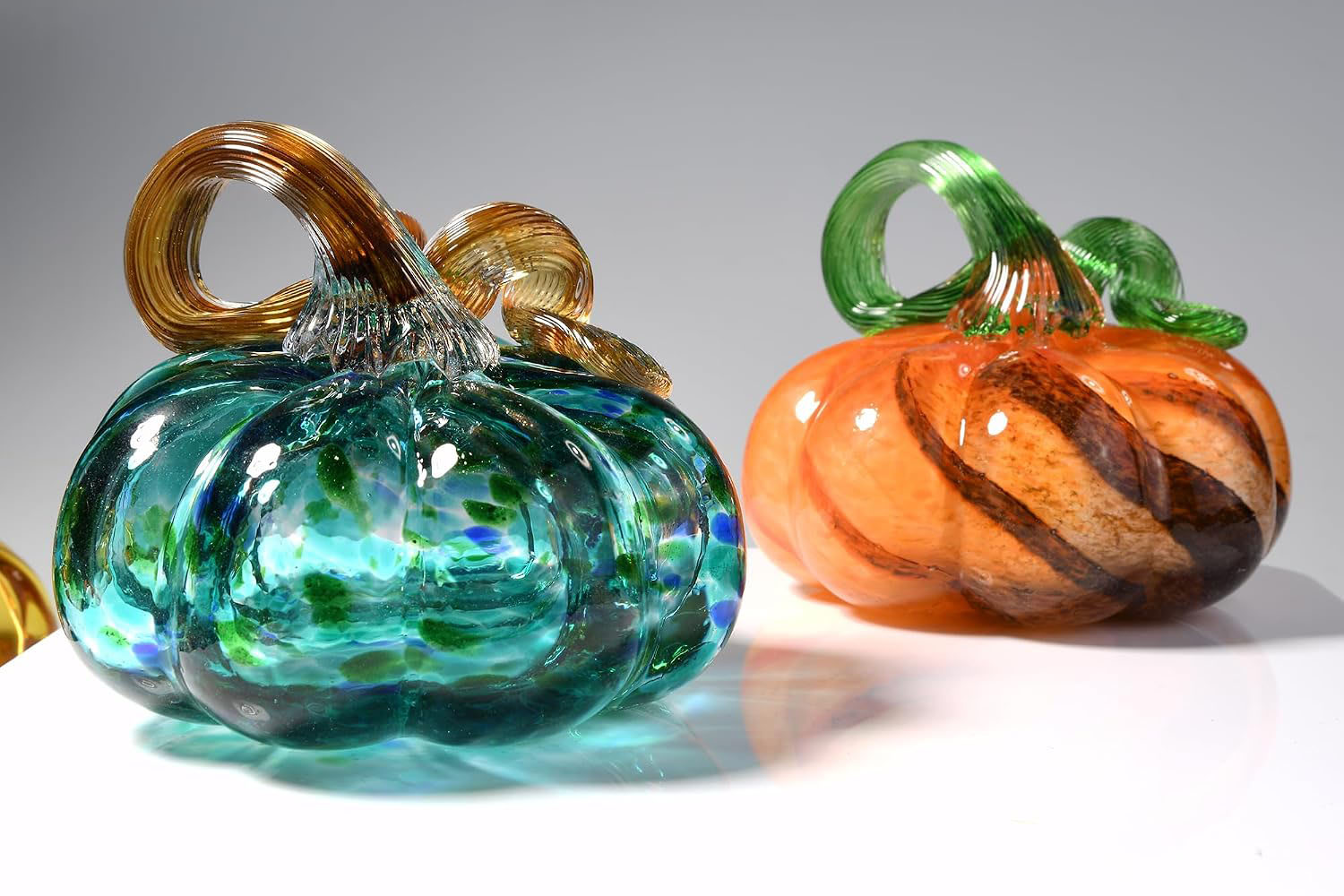 Orange-amber blown glass pumpkin, paired with a blue glass pumpkin, both with ribbed rounded shape and curved glass stem.