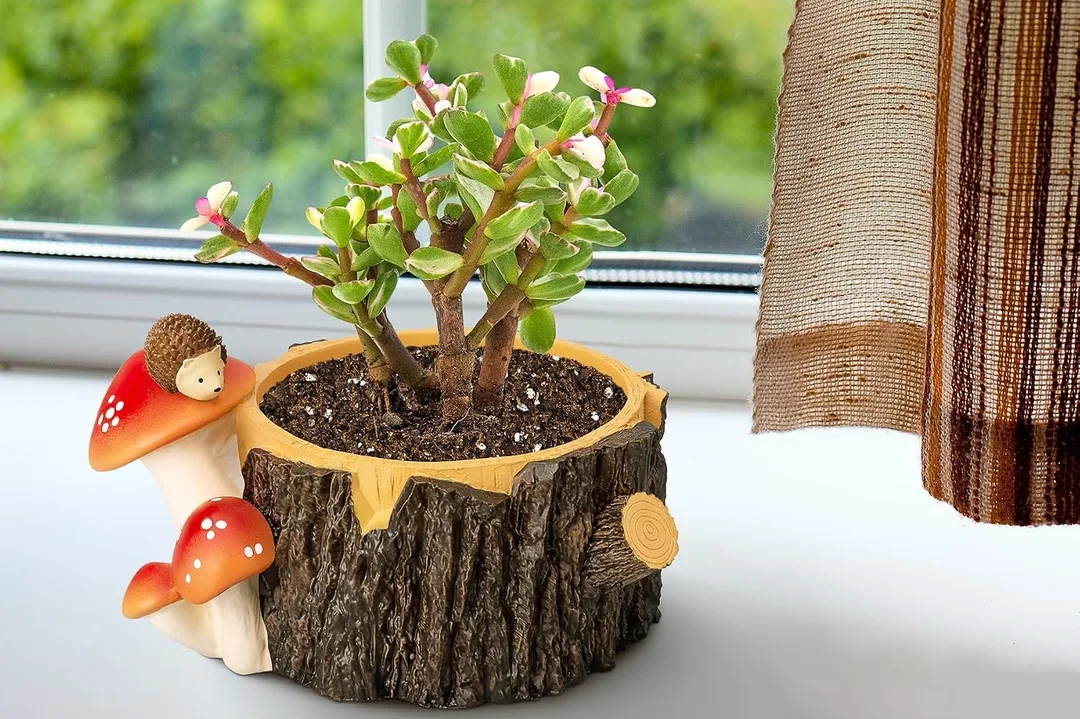 A tree stump planter with little mushrooms and a hedgehog on it with a live plant in the planter.