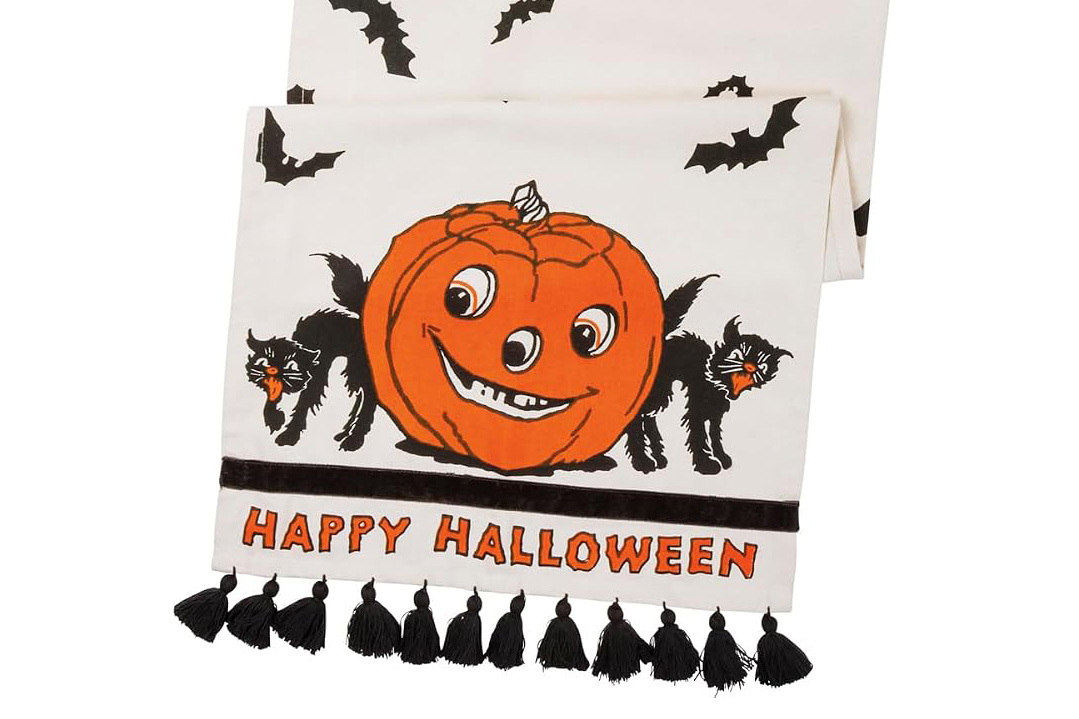 Retro Halloween table runner featuring an orange jack-o’-lantern, black cats, bats, “Happy Halloween” lettering, and black tassels.