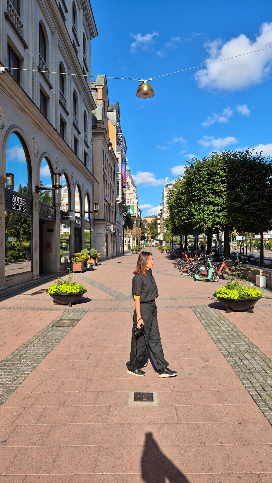 Woman wearing a siduro top and wide-leg trousers on a sunny city street.