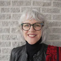 Michelle Clemens' headshot. Michelle is a white woman with chin-length white hair and glasses. She is in front of a brick wall and smiling at the camera.