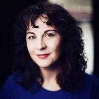 Olivia Heaney's headshot. Olivia is a white woman with shoulder-length curly black hair. She is smiling at the camera.