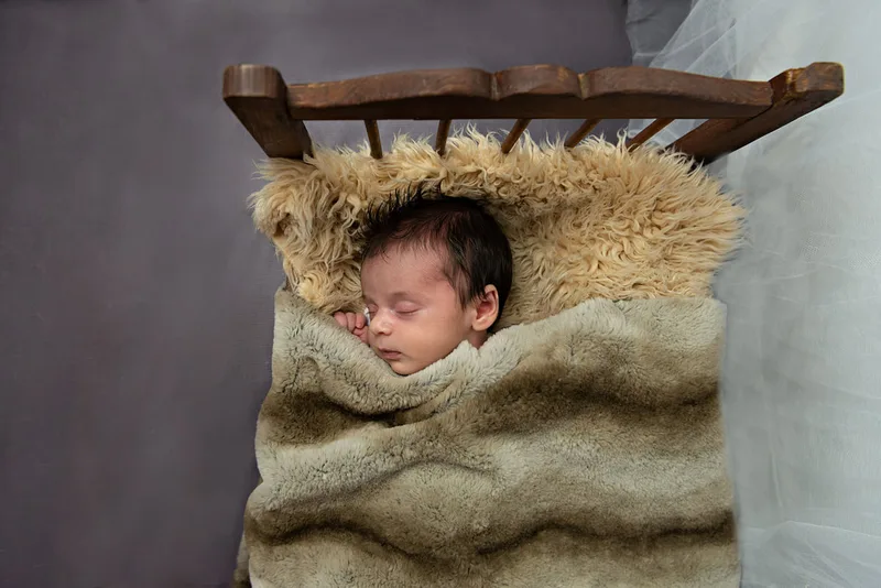 color photo of a baby newborn girl shot from above in a vintage doll bed