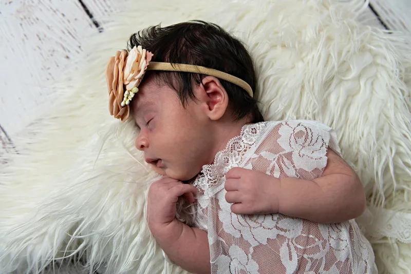 color photo of a baby newborn girl in a white lace outfit with a flower headband
