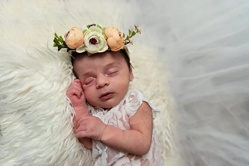 color photo of a baby newborn girl with a white lace outfit and a flower headband