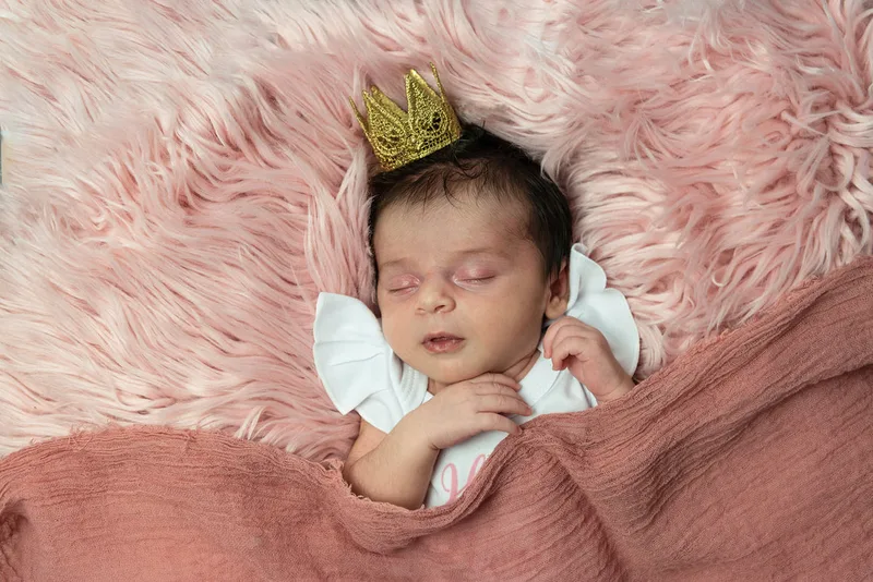 color photo of a baby newborn girl with a gold crown on laying on a pink fur rug