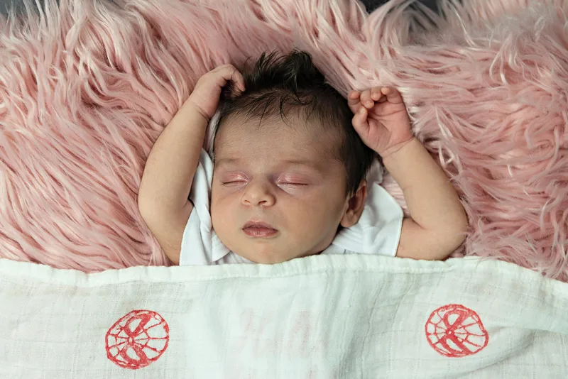 color photo of a baby newborn girl in a spiderman outfit laying on a pink fur rug