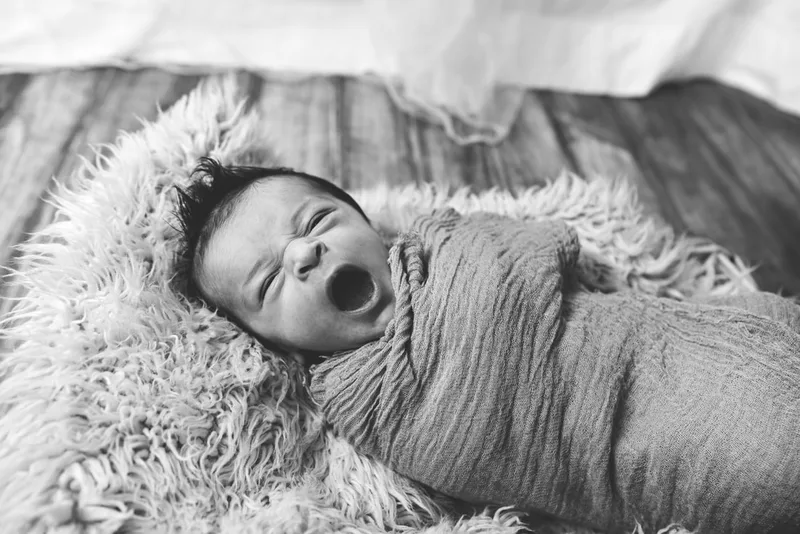 black and white photo of a baby newborn girl wrapped in a blanket on a fur rug