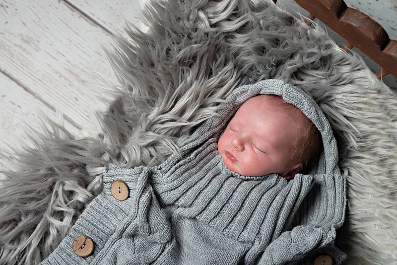 Color photo of a newborn baby boy in a grey knit sack. The photo is by Laura Pea Photography, a Long Island newborn and pet photographer. 