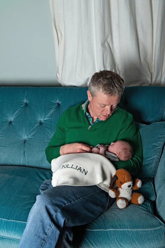 Color photo of a newborn baby boy being held by his father who looks down at him. The photo is by Laura Pea Photography, a Long Island newborn and pet photographer. 