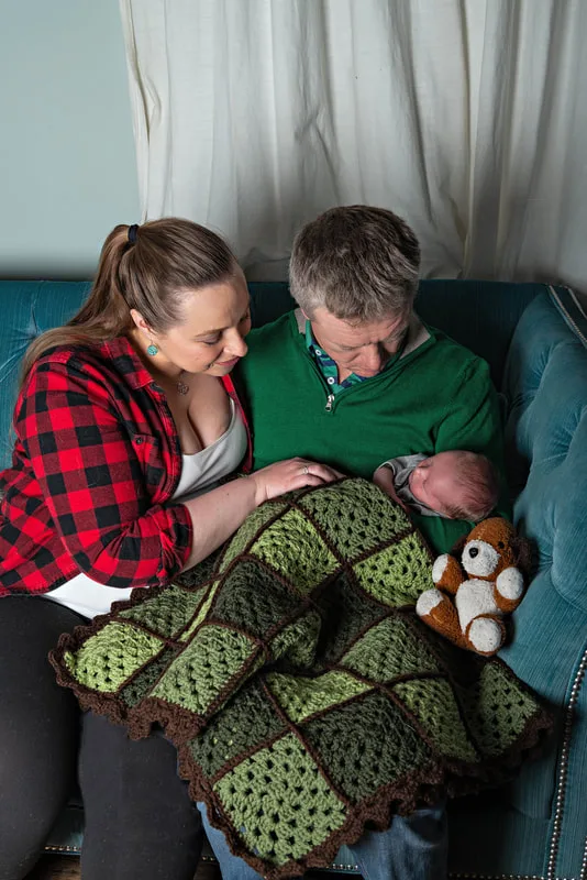 Color photo of a newborn baby boy being held by his parents who look down at him. The photo is by Laura Pea Photography, a Long Island newborn and pet photographer. 
