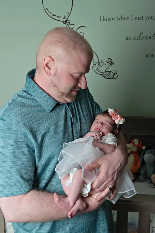 Color photo of a newborn baby girl being held by her dad in her Winnie the Pooh themed nursery. The photo was taken by Laura Pea Photography, a Long Island newborn and pet photographer. 