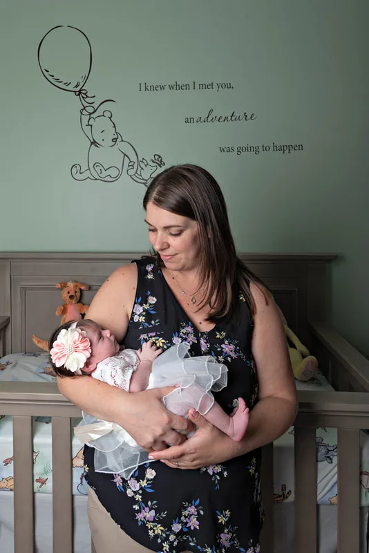 Color photo of a newborn baby girl being held by her mom in her Winnie the Pooh themed nursery. The photo was taken by Laura Pea Photography, a Long Island newborn and pet photographer. 