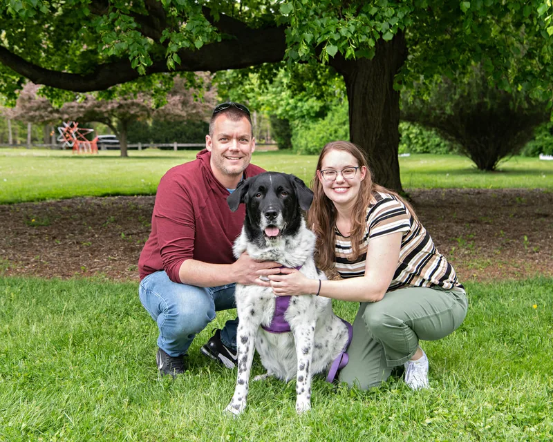 color photo of a black and white mix dog with his owners taken at a pet portrait program on the lawn of Comsewogue Public Library. The photo was taken by Laura Pea Photography, a Long Island pet photographer. 