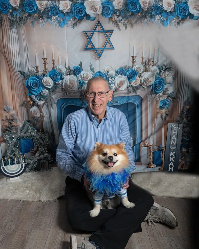 Color photo of a Pomeranian dog posing in front of Hanukkah holiday props. The photo was taken at Pawcasso in Westhampton Beach by Laura of Laura Pea Photography, a Long Island based pet photographer. 