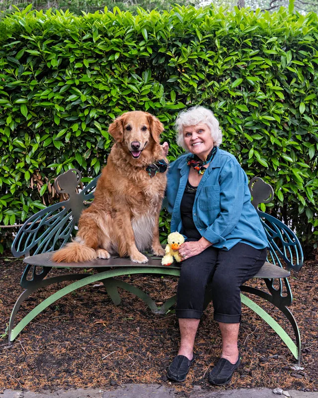 A color photo of a golden retriever dog and a woman. The photo was taken by pet photographer Laura Paesano of Laura Pea Photography for a pet portrait program held by the Middle Country Public Library in their outdoor Nature Explorium. 