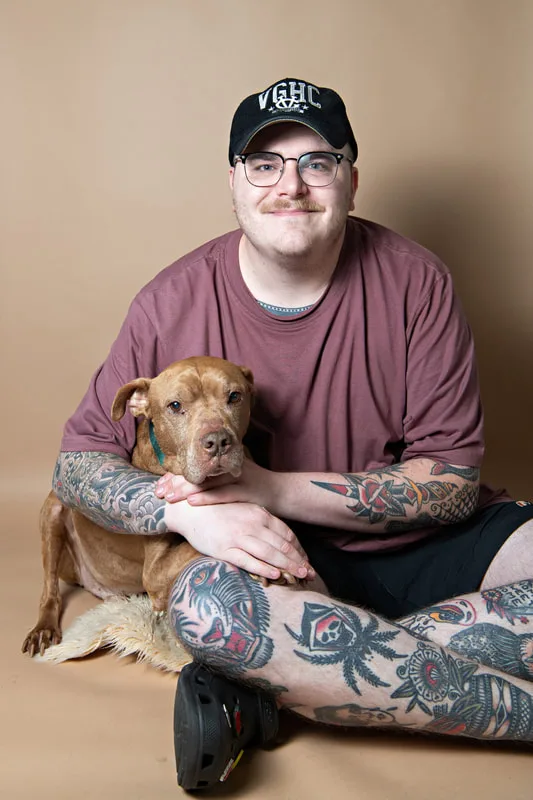 Color photo of a senior pit bull dog against a light brown paper backdrop with his owner. The photo was taken in the studio of Laura Pea Photography, a Long Island based pet photographer. 