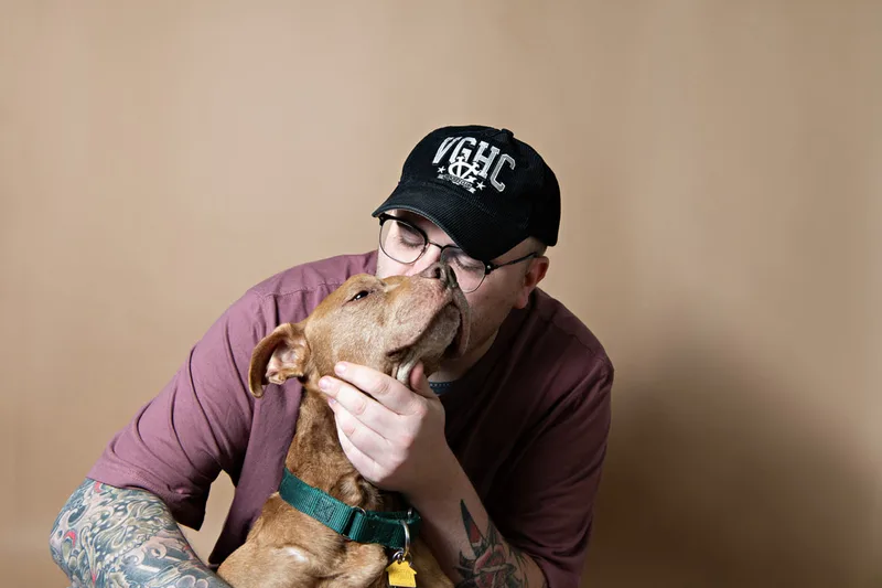 Color photo of a senior pit bull dog against a light brown paper backdrop with his owner. The photo was taken in the studio of Laura Pea Photography, a Long Island based pet photographer. 