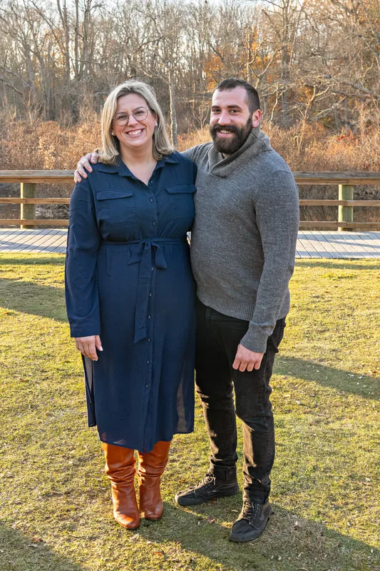 Color photo of a sister and brother posing outside on a lawn. 