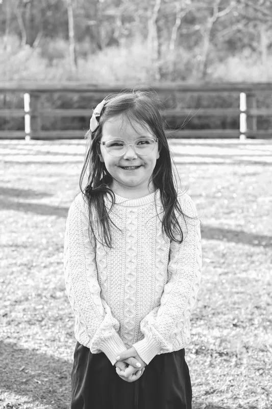 Black and white photo of a 5 year old girl standing outside on a lawn.