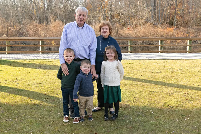 Color photo of grandparents with their three grandkids standing outside on a lawn.