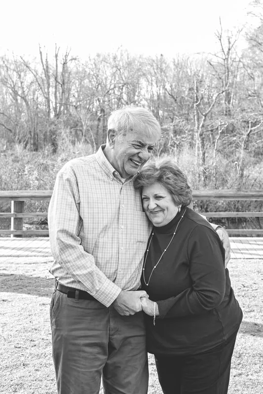 Black and white photo of a husband and wife laughing together standing outside on a lawn.