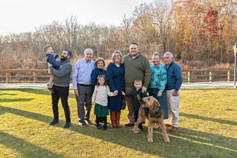 Color photo of a group extended family photo with mom, dad, both sets of grandparents, uncle, three kids and a dog.