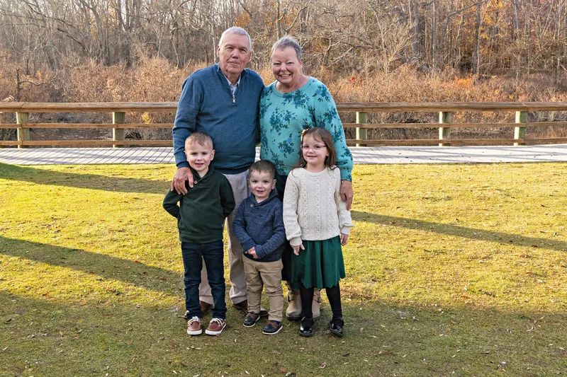 Color photo of grandparents with their three grandkids standing outside on a lawn.
