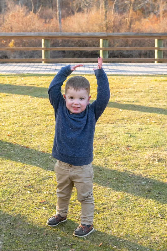 Color photo of a 2 year old boy smiling with his hands above his head