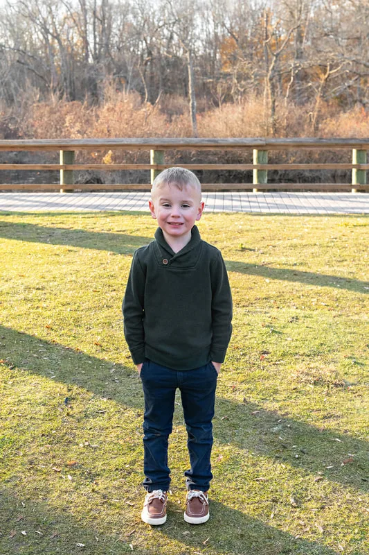 Color photo of a 5 year old boy standing outside on a lawn.