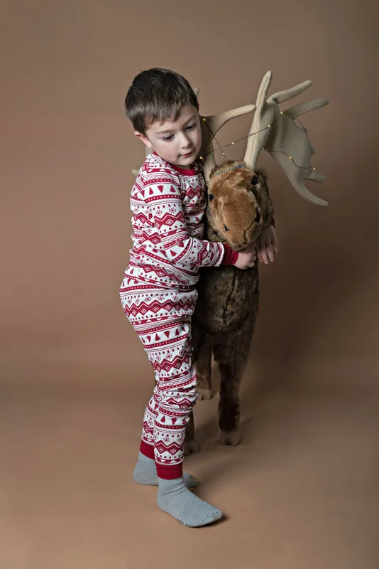 A color photo of a four year old white boy hugging a big stuffed moose in front of a light brown paper backdrop. The photo was taken by Laura Pea Photography, a Long Island based photographer. 