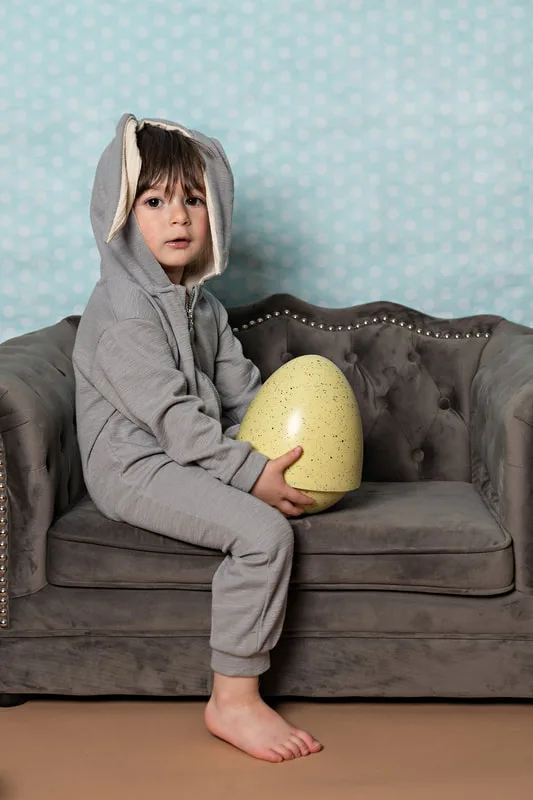 Toddler boy dressed in an Easter bunny costume holding a big yellow egg looking at the camera