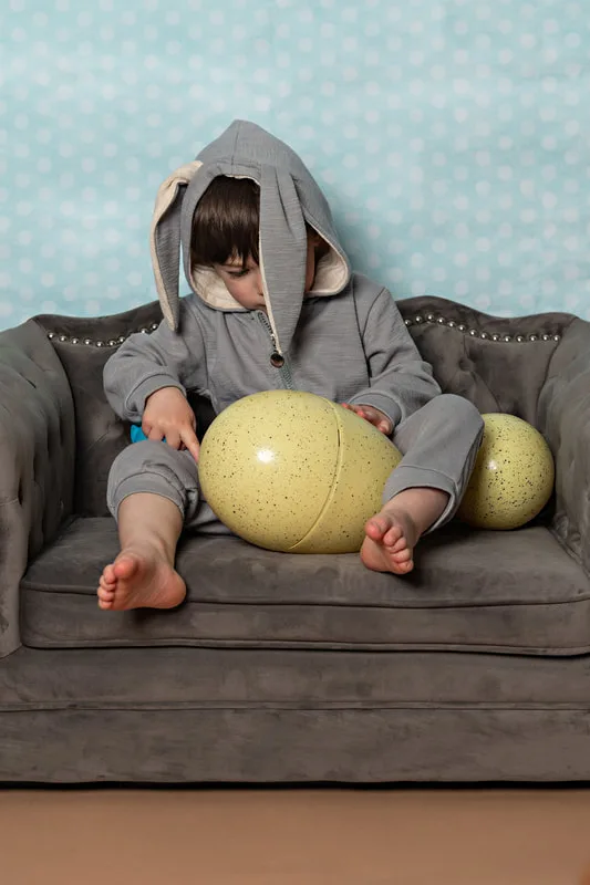 Toddler boy dressed in an Easter bunny costume holding a big yellow egg looking down at it