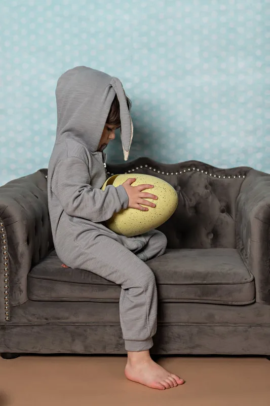 Toddler boy dressed in an Easter bunny costume holding a big yellow egg from the side