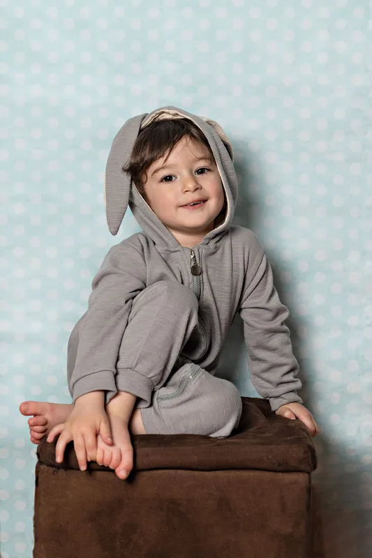 Toddler boy dressed in an Easter bunny costume sitting on a stool smiling at the camera