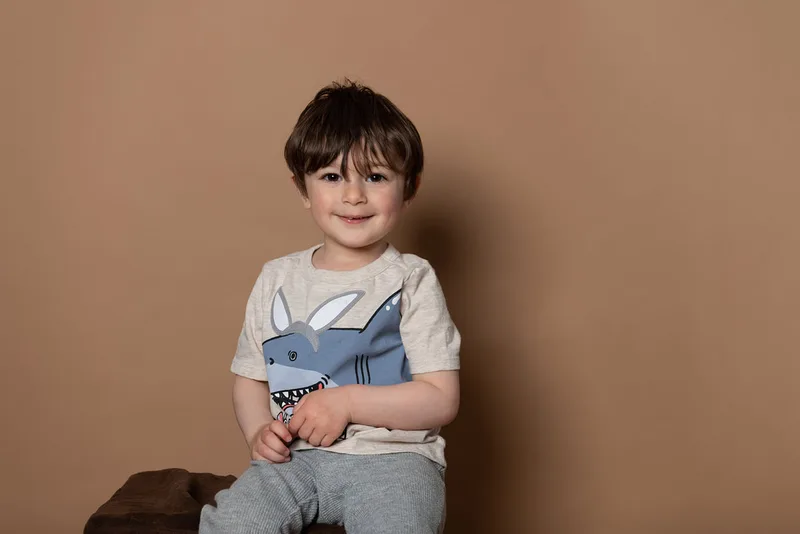 Toddler boy wearing a shirt with a shark dressed as an Easter bunny smiling at the camera