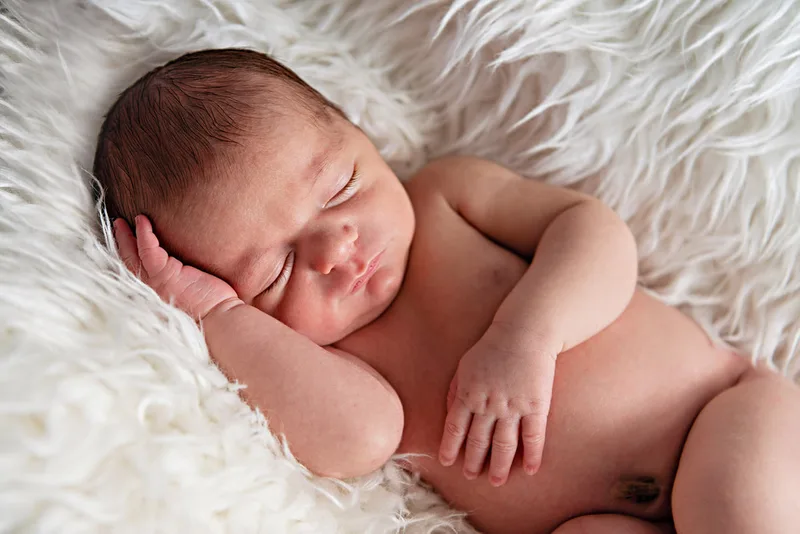 photo of a newborn baby boy laying on a white furry rug