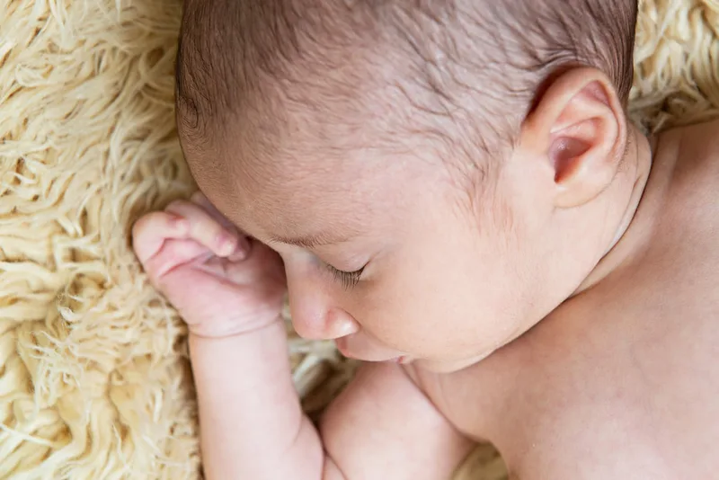 Color close up photo of a newborn baby laying on a beige furry rug photographed in a studio. The photo was taken by Laura Pea Photography, a Long Island based newborn photographer.